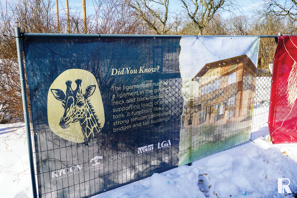 Construction fence banner showing a giraffe illustration, a fact about giraffe neck anatomy, a building rendering, and project partner logos.