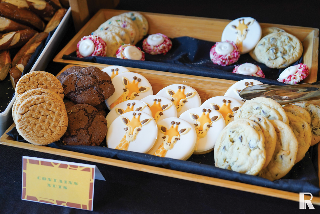 Wooden trays filled with assorted cookies, including giraffe-decorated sugar cookies and a sign labeled “contains nuts.”