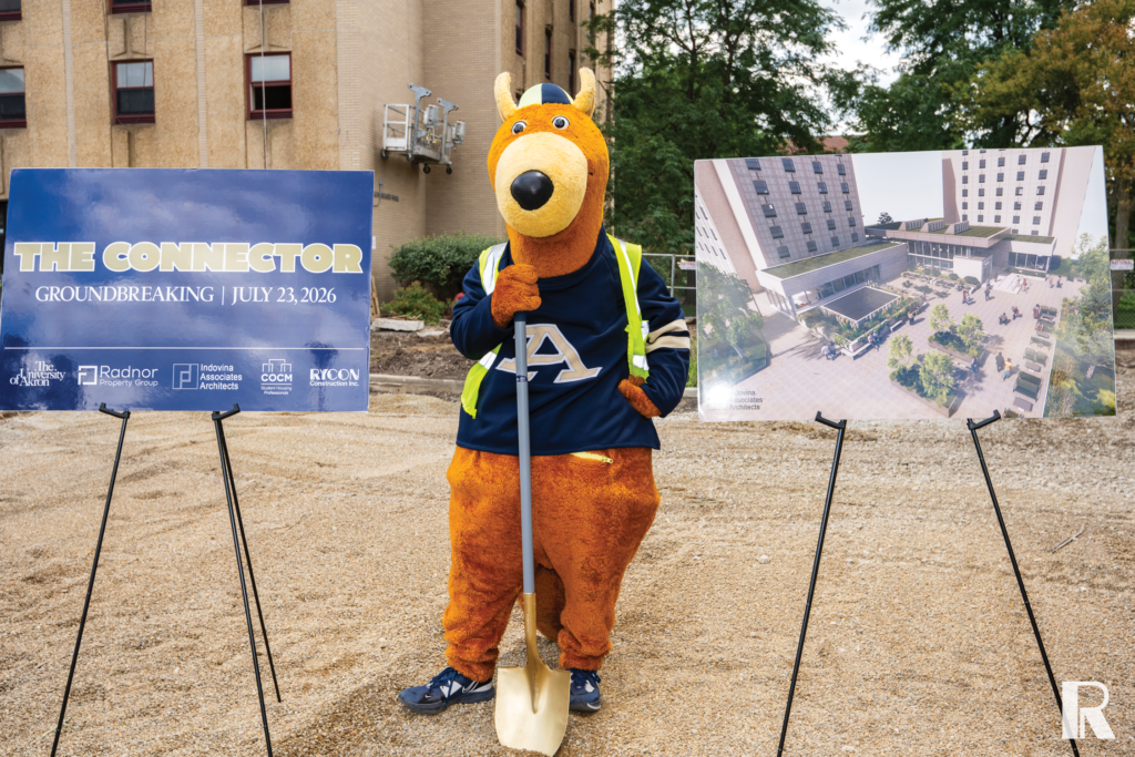 University of Akron mascot Zippy the Kangaroo stands with a golden shovel between a groundbreaking sign for “The Connector” and an architectural rendering of the new building.