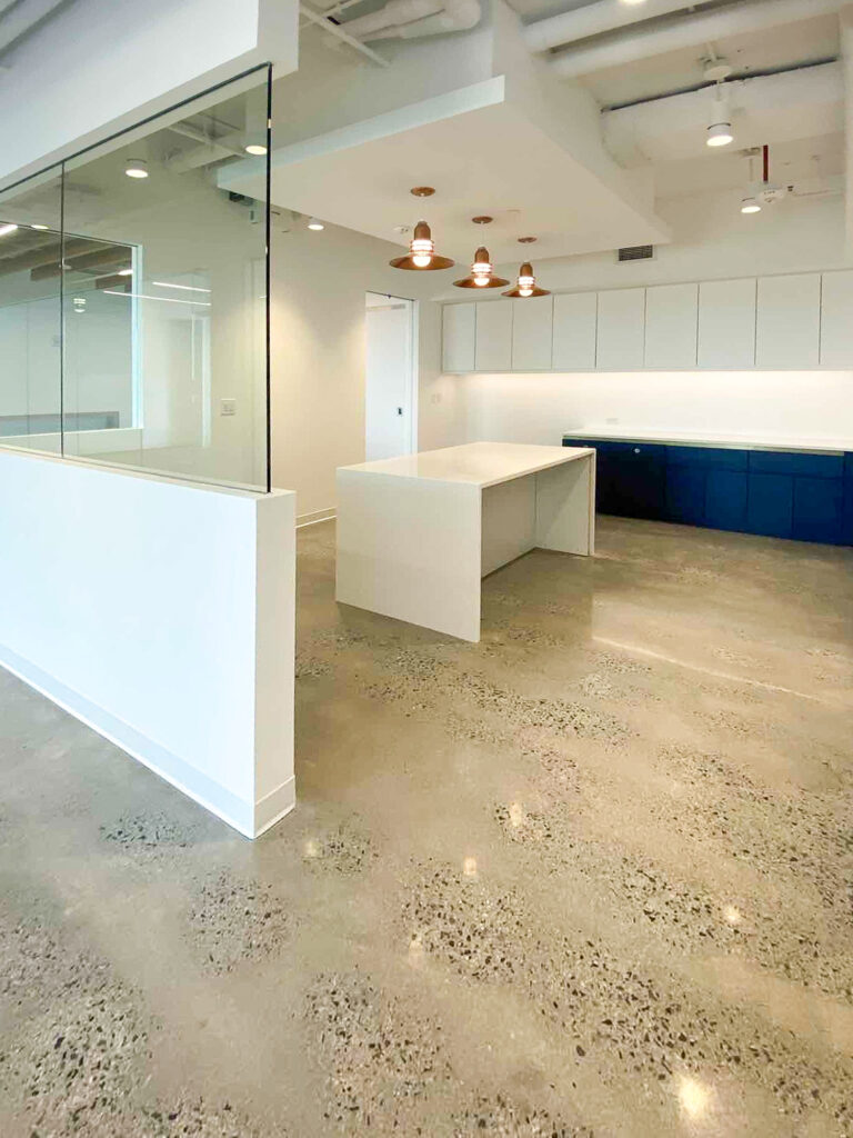 Modern office kitchenette with a white island, blue cabinets, and polished concrete floors.