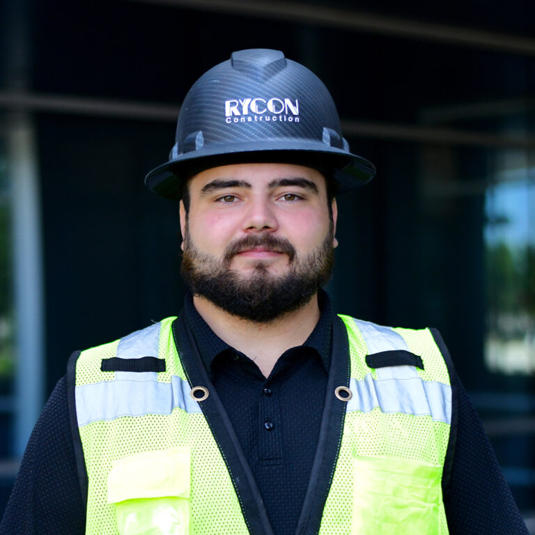 A man with a beard wearing a Rycon Construction hard hat and a high-visibility safety vest.