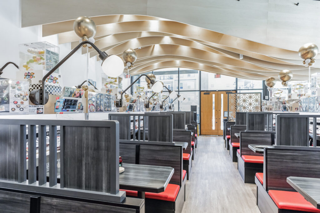 Restaurant interior with rows of booths featuring dark wood partitions and red bench seating, under curved wooden ceiling beams.