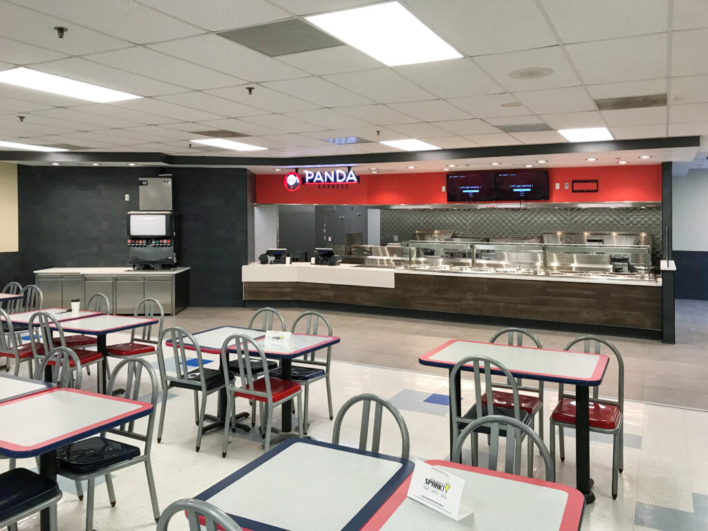 The interior of a Panda Express restaurant featuring a service counter, a soda fountain, and several tables with gray and red chairs.