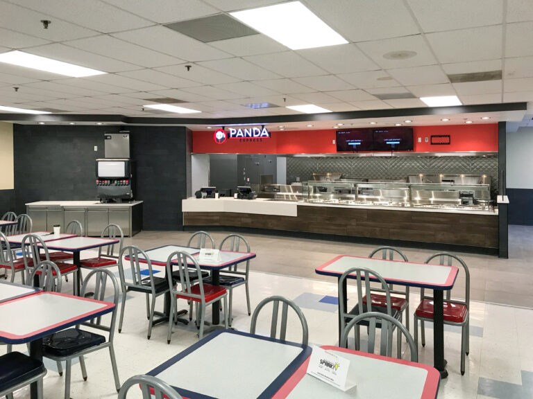 The interior of a Panda Express restaurant featuring a service counter, a soda fountain, and several tables with gray and red chairs.