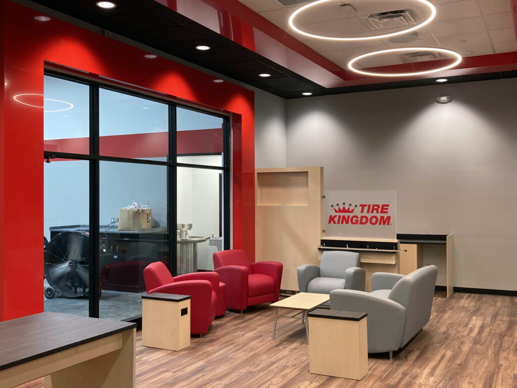 Waiting area of a Tire Kingdom service center with red and gray armchairs, a small table, and a branded sign.