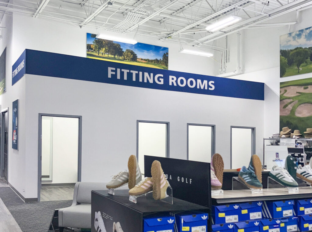 Fitting room entrance inside a store, with several pairs of Adidas sneakers displayed on racks in the foreground.