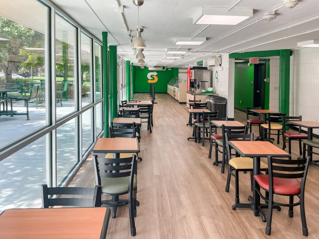 Interior of a Subway restaurant with tables, chairs, and large windows looking out to a patio.