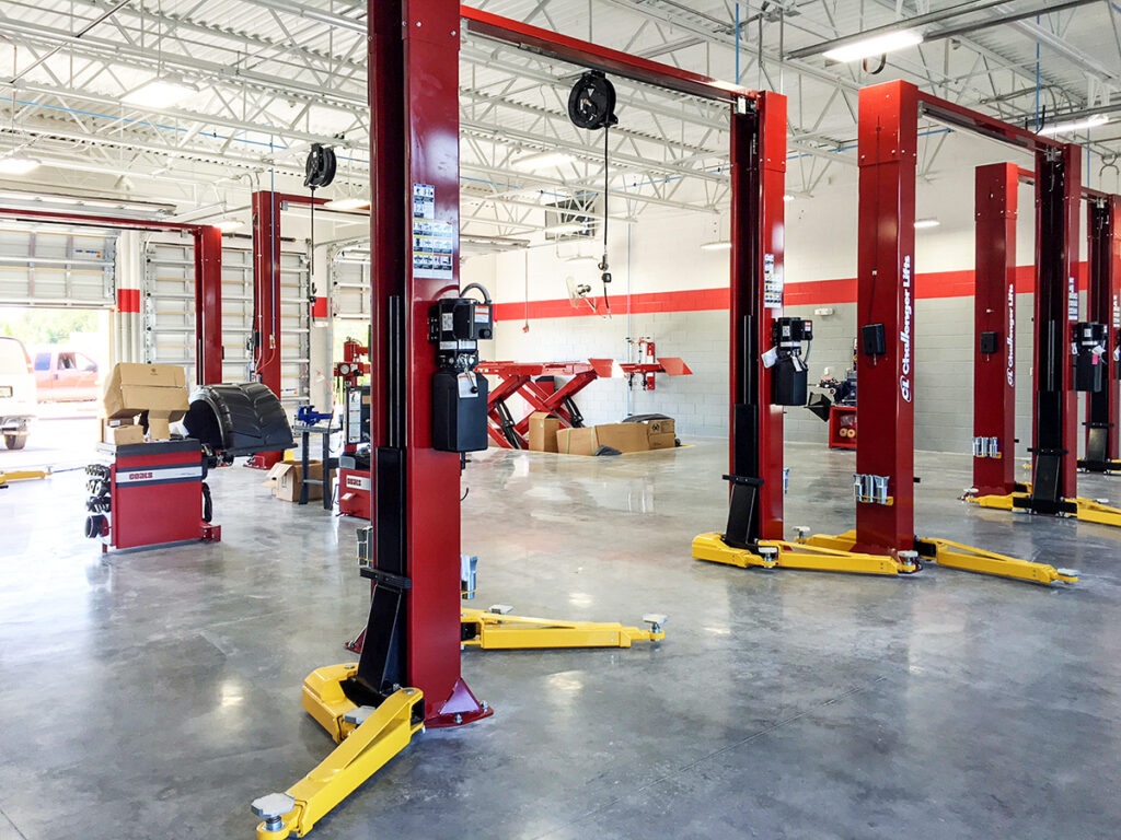 An auto repair shop interior featuring several red two-post vehicle lifts on a concrete floor.