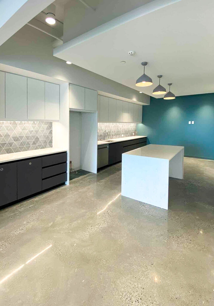 Modern kitchen featuring dark base cabinets, white upper cabinets, a geometric patterned backsplash, and a white central island against a teal accent wall.