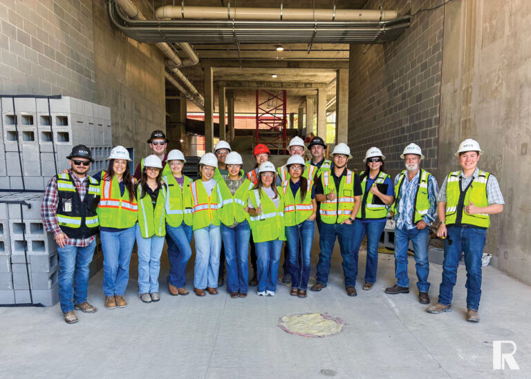 A group of construction workers in hard hats and high-visibility vests posing for a photo inside an unfinished concrete building.