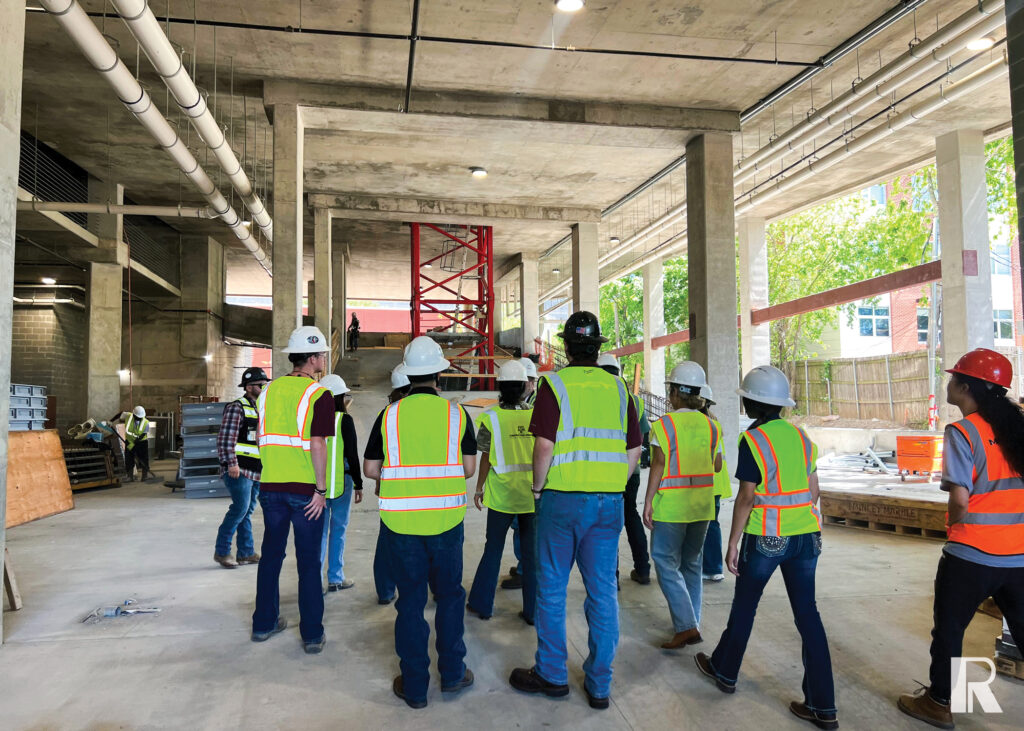 A group of people wearing hard hats and high-visibility safety vests standing inside a concrete construction site.