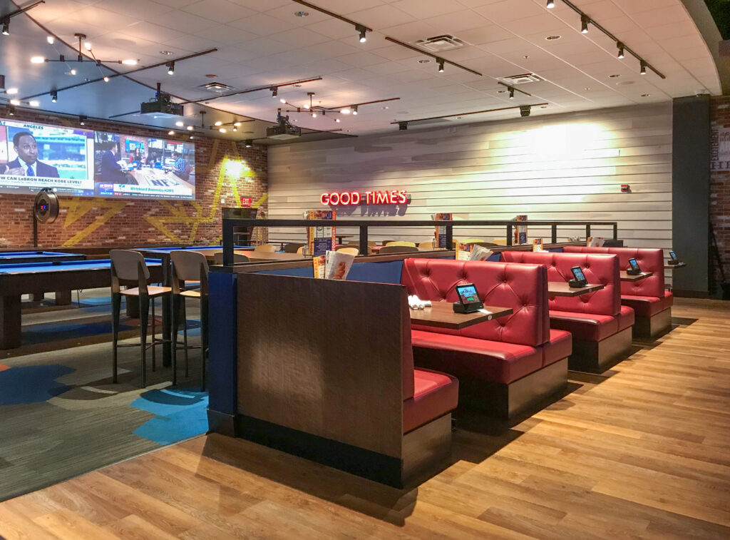 Restaurant interior featuring red tufted booths, pool tables, and a large television screen displaying a sports broadcast.