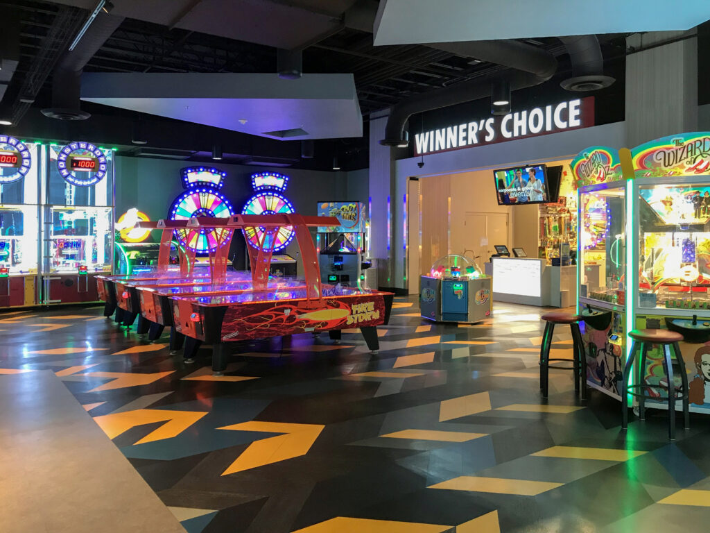 Arcade interior featuring air hockey tables, various game machines, and a “Winner’s Choice” prize counter.