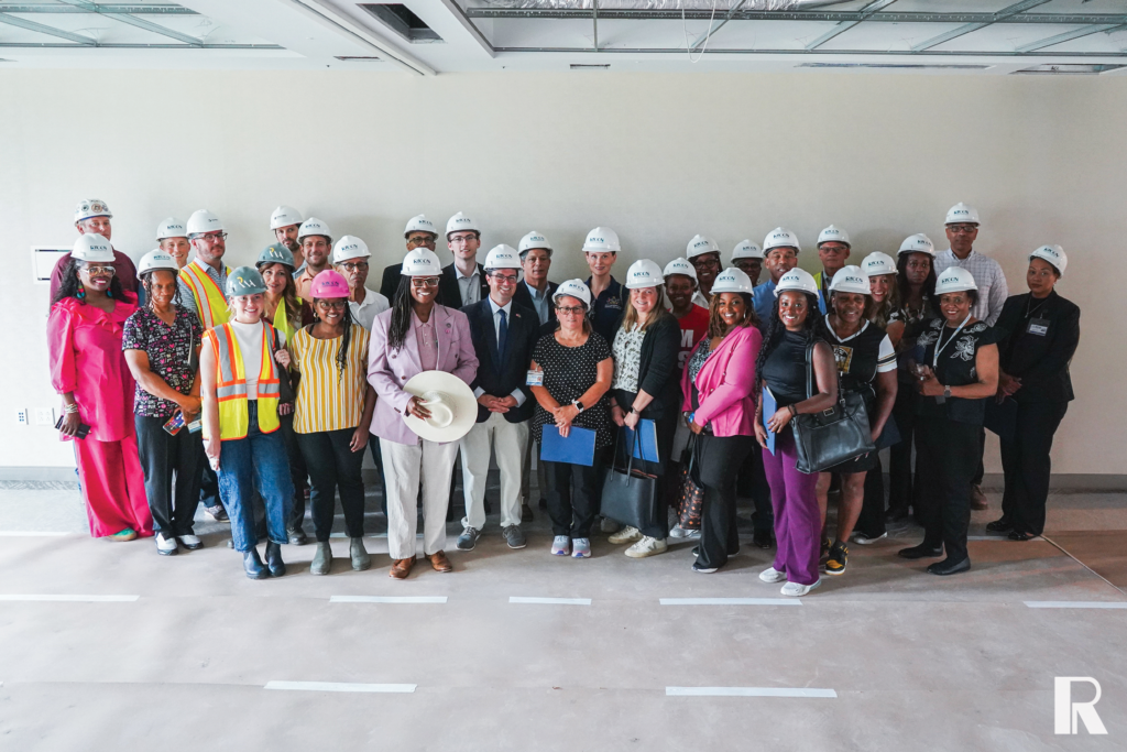 A large group of diverse people wearing white hard hats stand together in a construction site.