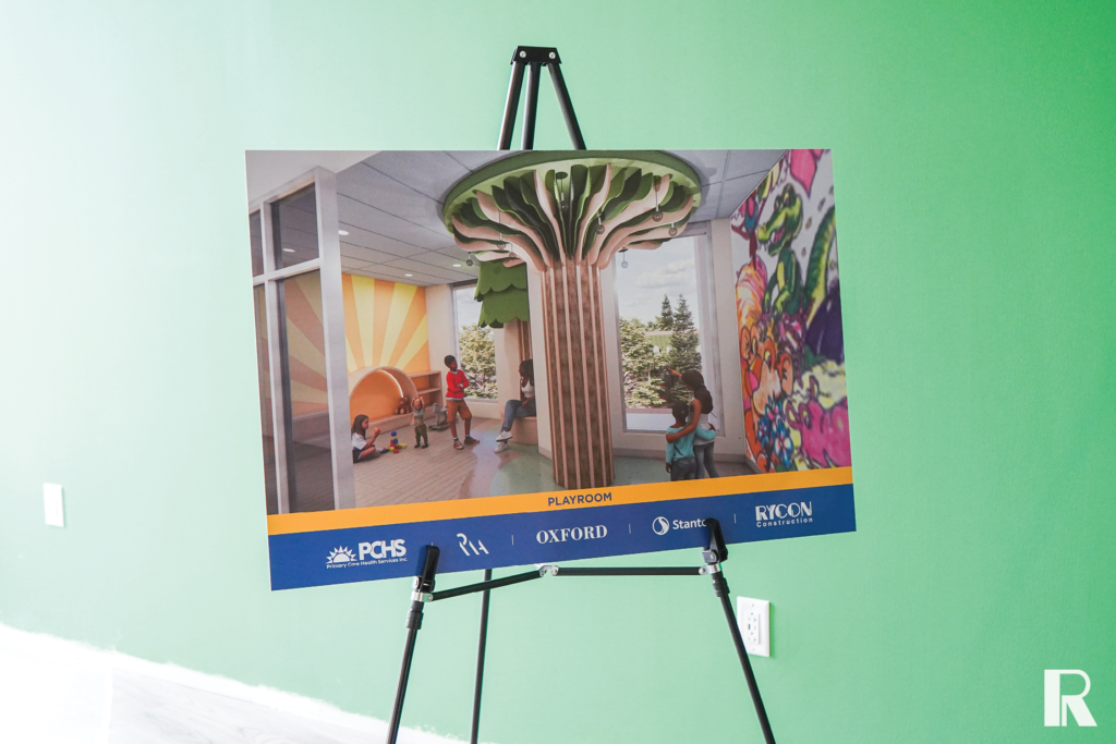 An easel displays a rendering of a pediatric playroom featuring a central tree-shaped structure, a mural, and a lounge area, with logos for PCHS, Oxford, and Rycon Construction at the bottom.