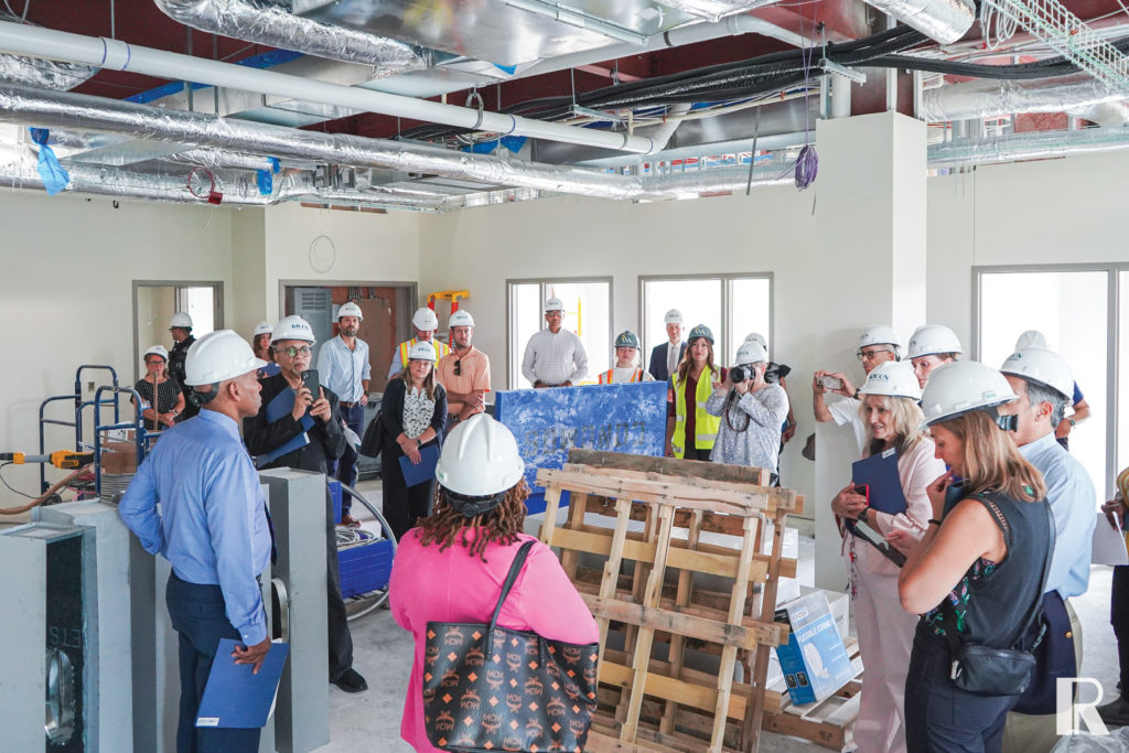 A large group of people wearing hard hats and professional attire during a tour of a construction site.