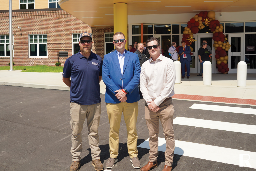 Three men stand in front of a school entrance decorated with a balloon arch.
