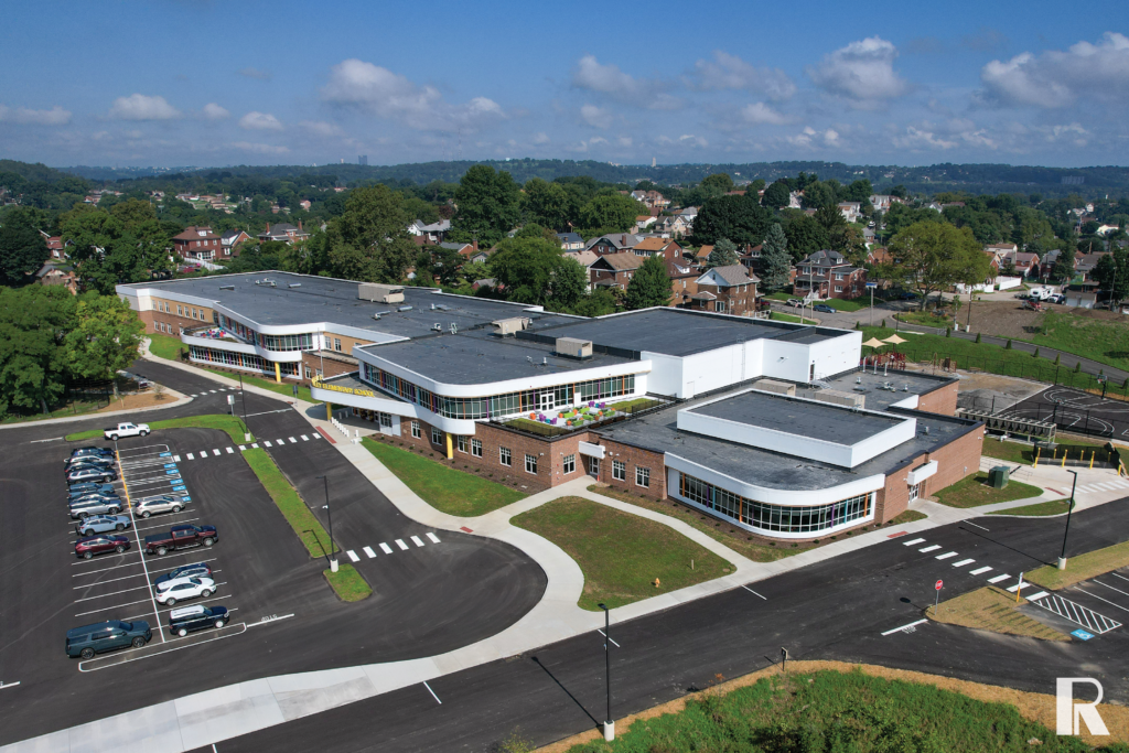 Aerial view of a large modern school building with a parking lot and surrounding residential neighborhood.