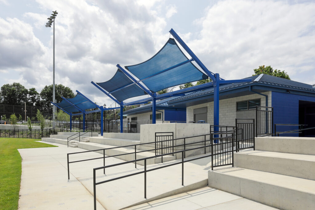 Concrete stadium seating and ramps with blue fabric shade structures in front of a building.