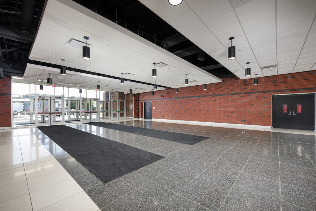 A spacious, empty building lobby with tile floors, a long brick wall, and glass entrance doors.