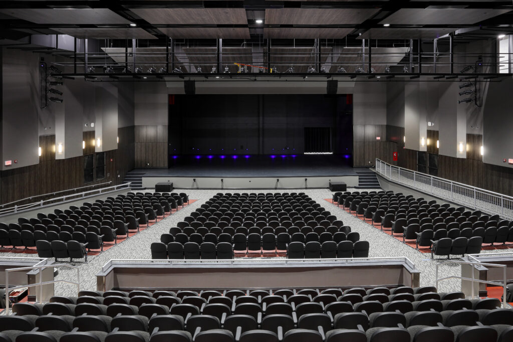 An empty modern auditorium with rows of tiered seating facing a dark stage.