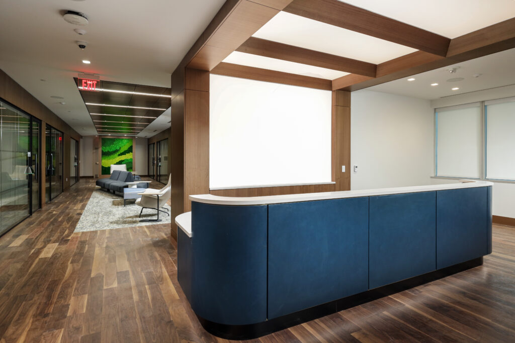 A blue reception desk in a modern office lobby with a wooden ceiling feature and a seating area in the background.