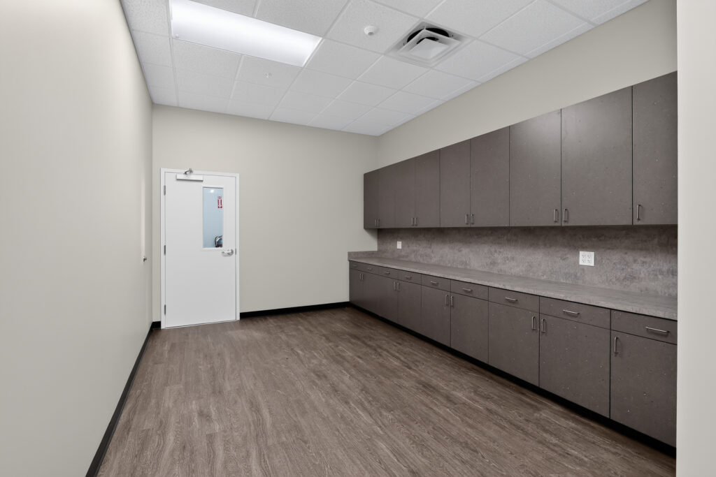An empty office room with dark grey cabinets and wood-look flooring.