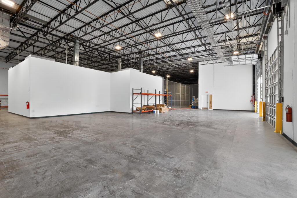 An empty warehouse space with concrete floors, white partition walls, and exposed ceiling trusses.