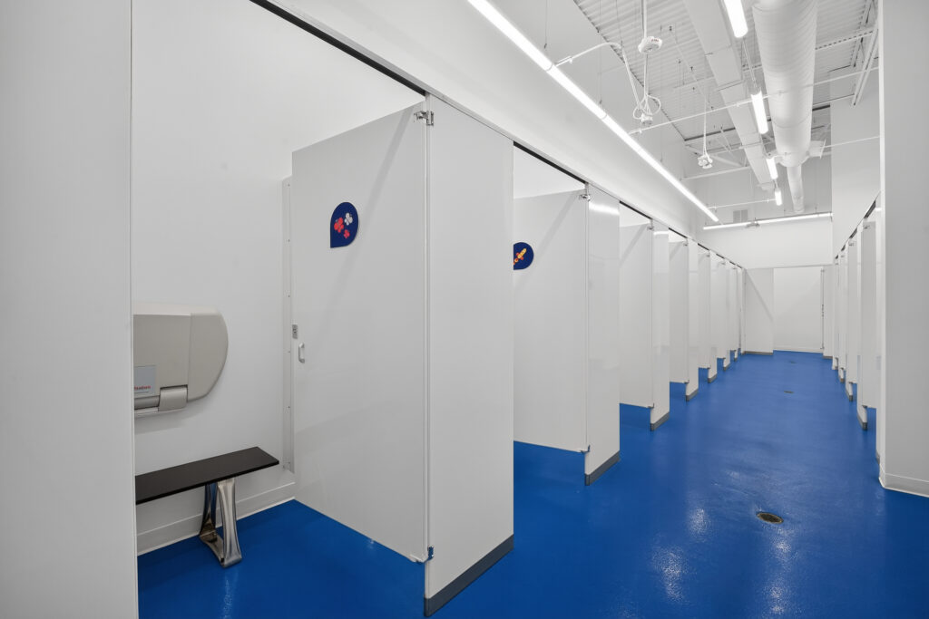 A row of white bathroom stalls with blue floors and a wall-mounted changing station.
