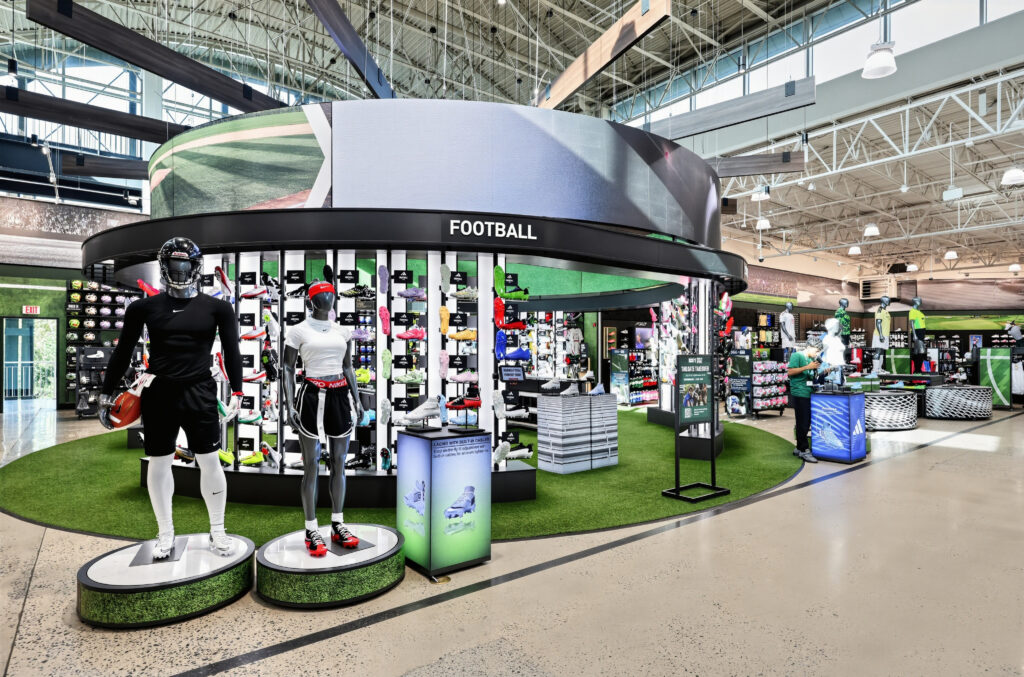 A football section in a sporting goods store featuring mannequins in athletic gear and displays of cleats.