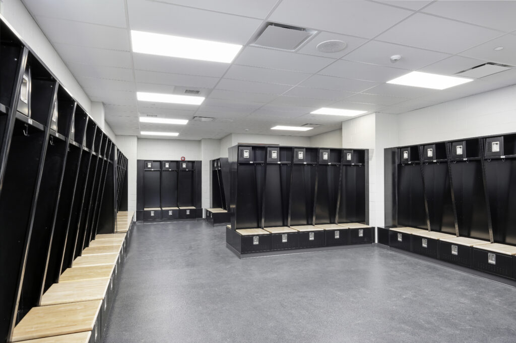 Empty locker room with rows of black lockers and light wood benches on a grey floor.