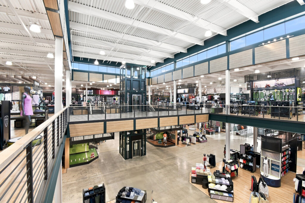 Interior view of a large, multi-level sporting goods store with an elevator, clothing displays, and merchandise racks.