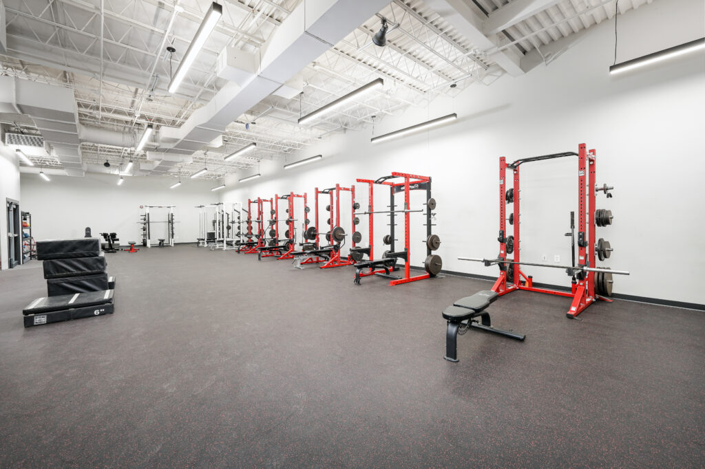 A row of red squat racks and weight benches inside a gym.