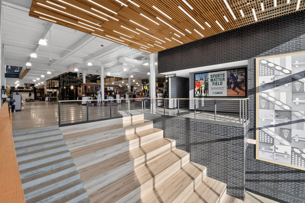 Staircase leading to a retail store interior with a sign titled “Sports Matter Field” mounted on a brick wall.