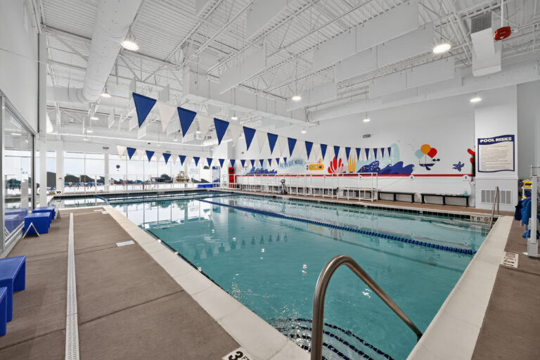 Indoor swimming pool with blue lane markers, hanging triangular flags, and a wall mural.