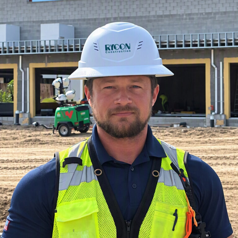 A construction worker in a hard hat and high-visibility vest stands in front of a building under construction.